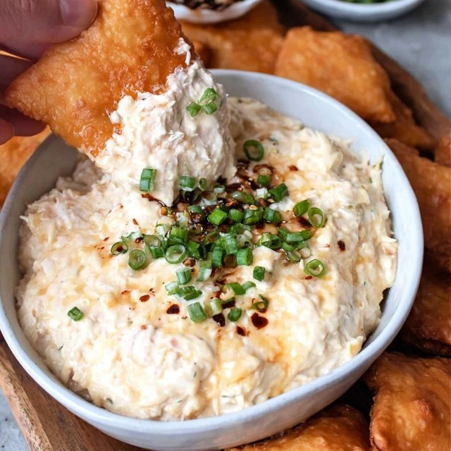 Creamy crab dip in a cast iron skillet, golden bubbly cheese top with browned spots, fresh chives and Old Bay seasoning sprinkled on top, served with crackers, baguette slices, and celery sticks around it