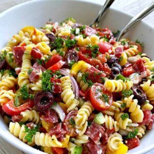 Italian pasta salad in a big bowl, rotini with salami, mozzarella balls, cherry tomatoes, bell peppers, olives and red onion in Italian dressing, parsley on top