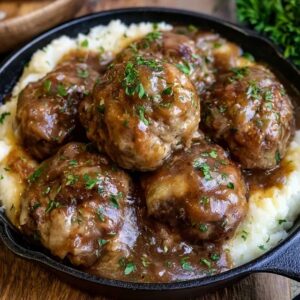 Meatballs and mashed potatoes on a plate, juicy browned beef meatballs smothered in rich brown gravy over a mound of creamy mashed potatoes, parsley garnish