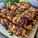 Grilled chicken skewers on a platter, charred marinated chicken chunks threaded with bell peppers, red onion and zucchini, sprinkled with parsley and lemon wedges